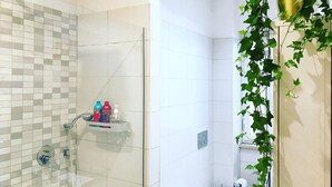 A modern bathroom with a glass shower enclosure, white tiled walls, and a shelf with toiletries. - Cozy Vintage Apartment in Trastevere within walking distance of downtown  (Roma)