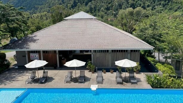A swimming pool with lounge chairs and umbrellas, a building with a tiled roof, and a lush green landscape in the background. - Rebungan Resort Langkawi (Langkawi)