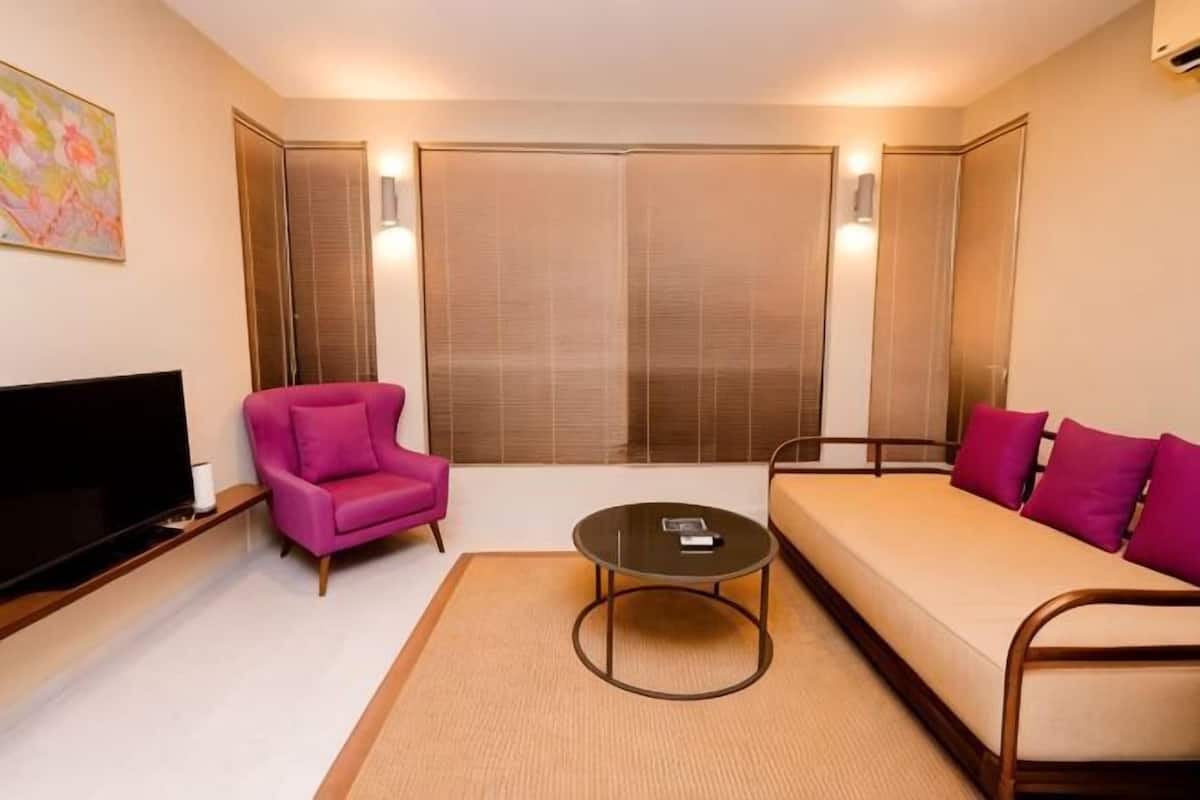 Habitació d'hotel moderna amb sofà, butaca, televisió de pantalla plana i una finestra gran amb persianes.