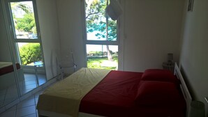 Ein Schlafzimmer mit Bett, Stuhl und Fenster mit Blick ins Grüne.