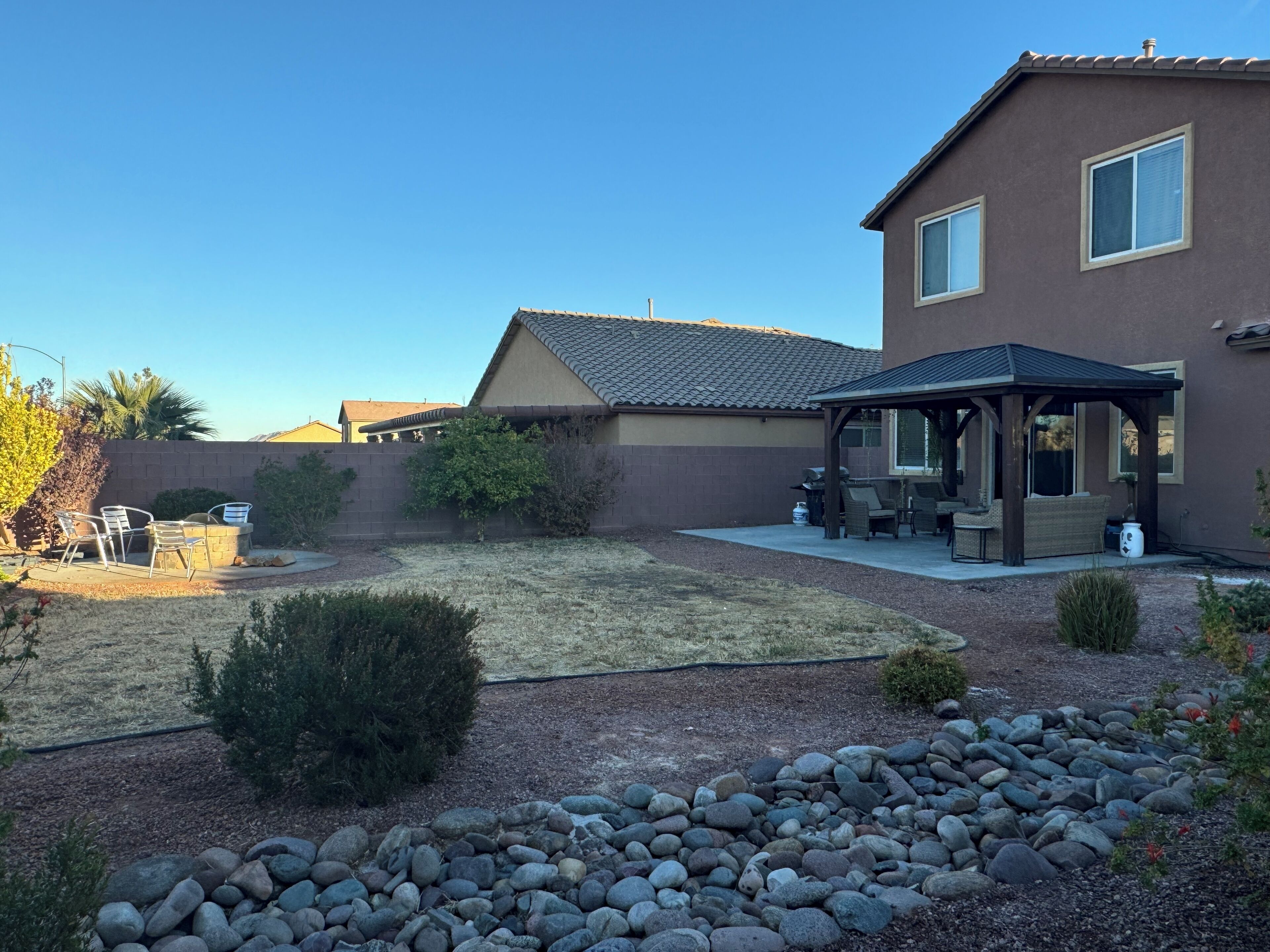 A residential backyard with a patio area, a covered seating area, and a stone pathway.