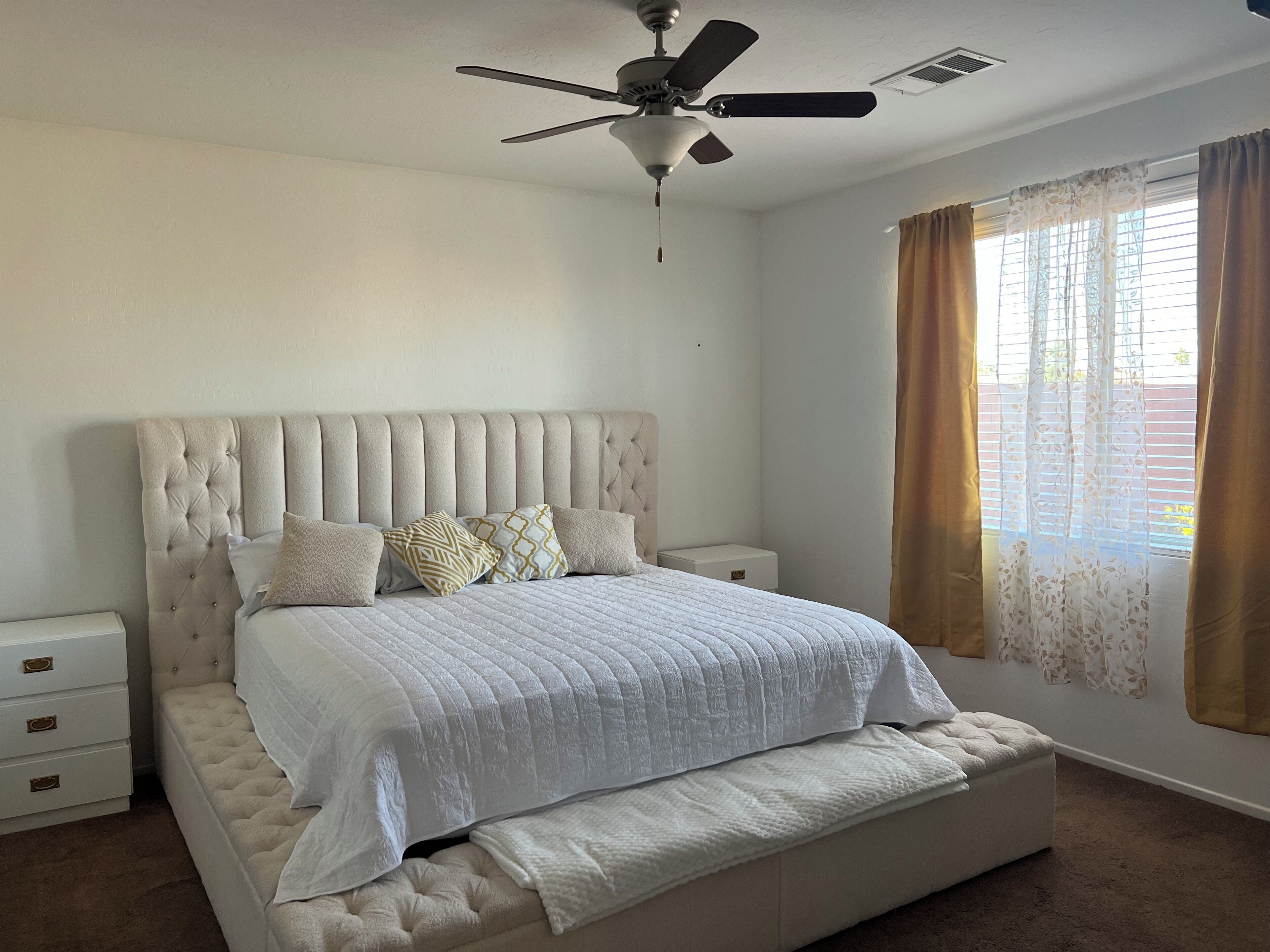 A bedroom with a tufted headboard, a bed with white bedding, a nightstand, and a ceiling fan.