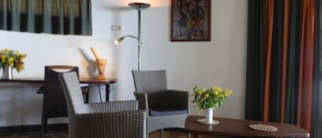 A room with wicker chairs, a small table with a vase of flowers, a floor lamp, and a painting on the wall.