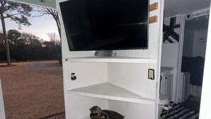 Ein Zimmer mit Fernseher auf einem weißen Regal, einem kleinen Korb und einer Tür zu einem Badezimmer.