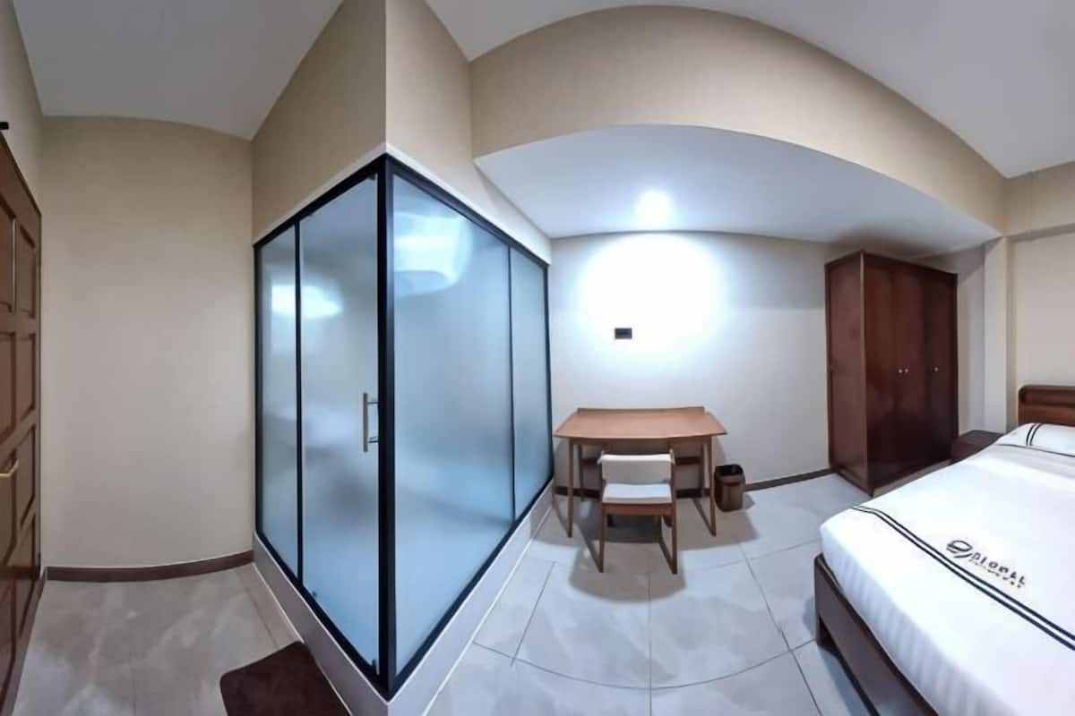 A bedroom with a bed, a desk, a chair, a wardrobe, and a glass partition.