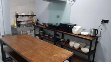 A kitchen with a wooden table, shelves with kitchenware, a microwave, and a kettle.