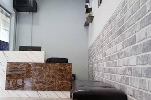 A reception area with a marble counter, a black leather bench, and a brick-patterned wall. - Global Residency (Kota Kinabalu)