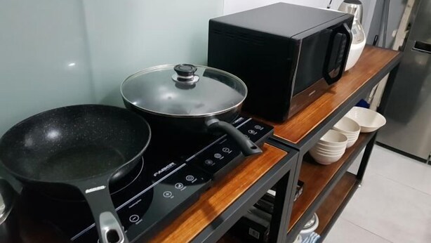 A kitchen with a stove, a microwave, a pot, and a microwave box on a wooden shelf. - Global Residency (Kota Kinabalu)