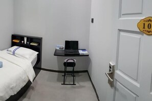 A hotel room with a bed, a desk with a laptop, a chair, and a door with a number plate. - Global Residency (Kota Kinabalu)