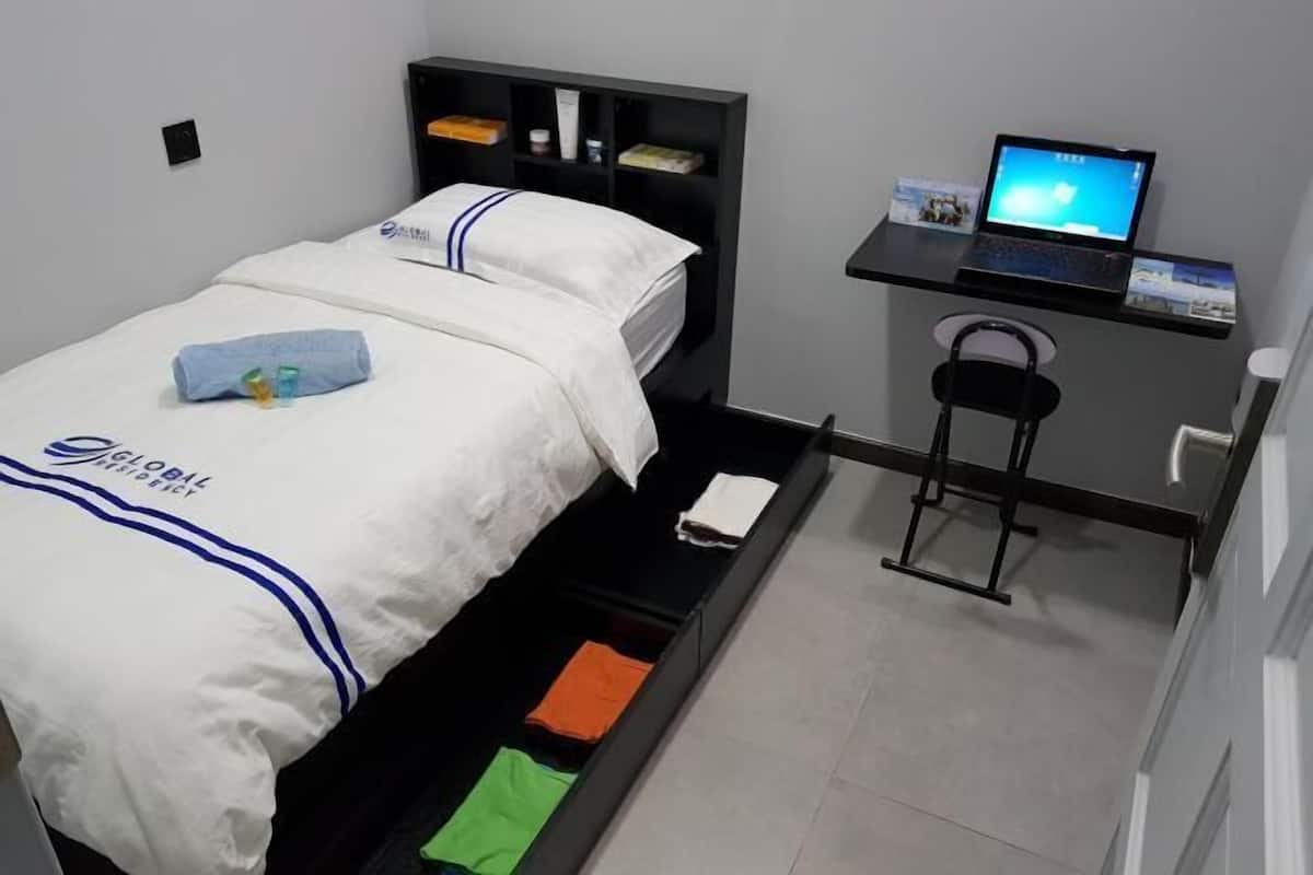 A hotel room with a bed, a desk with a laptop, and a shelf with toiletries.