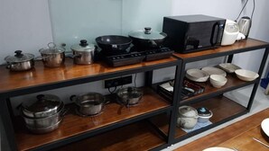 A kitchen with stainless steel pots, a black stove, a microwave, and various bowls and cups on shelves. - Global Residency (Kota Kinabalu)