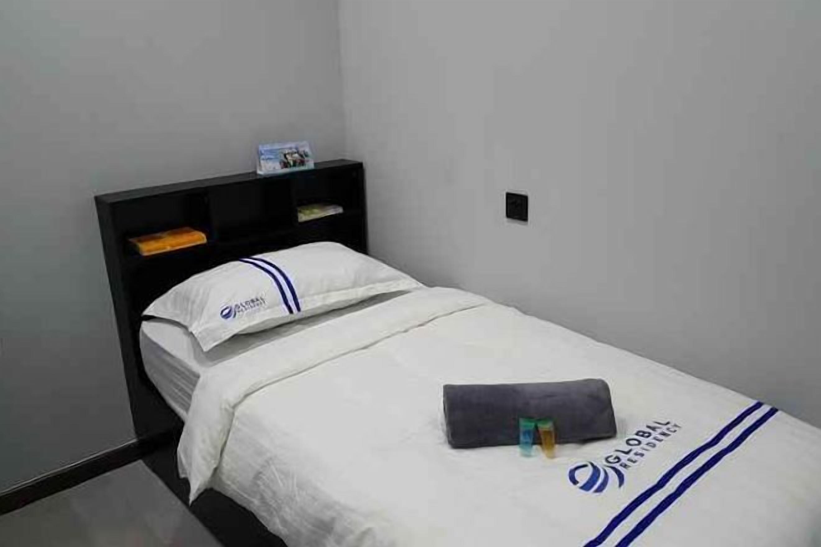 A single bed with a white bedspread and a pillow with a blue stripe.