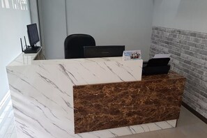 A reception desk with a marble top and a brown lower section, a black office chair, and a brick-patterned wall behind it. - Global Residency (Kota Kinabalu)