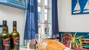 Un'area pranzo con due bottiglie di vino, bicchieri, un tavolo in legno, una panca, una pianta e un quadro raffigurante una barca a vela.