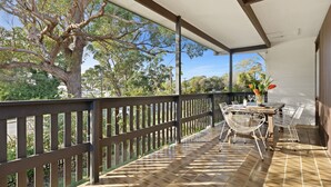 A covered outdoor patio with a table and chairs, surrounded by a wooden fence and a large tree.