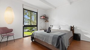 A modern bedroom with a large bed, a hanging light fixture, a chair, and a view of the outside.