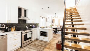 Una cocina moderna con armarios blancos, una campana extractora de acero inoxidable y una escalera de madera.