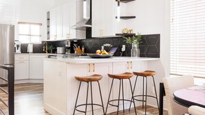 Una cocina moderna con armarios blancos, salpicadero negro y una isla central con taburetes.