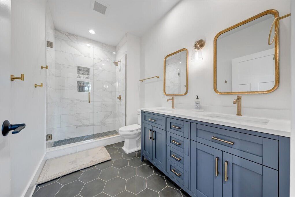 Een moderne badkamer met een douchecabine van glas, een wit toilet en een wastafelmeubel met een blauwe kast en gouden details.