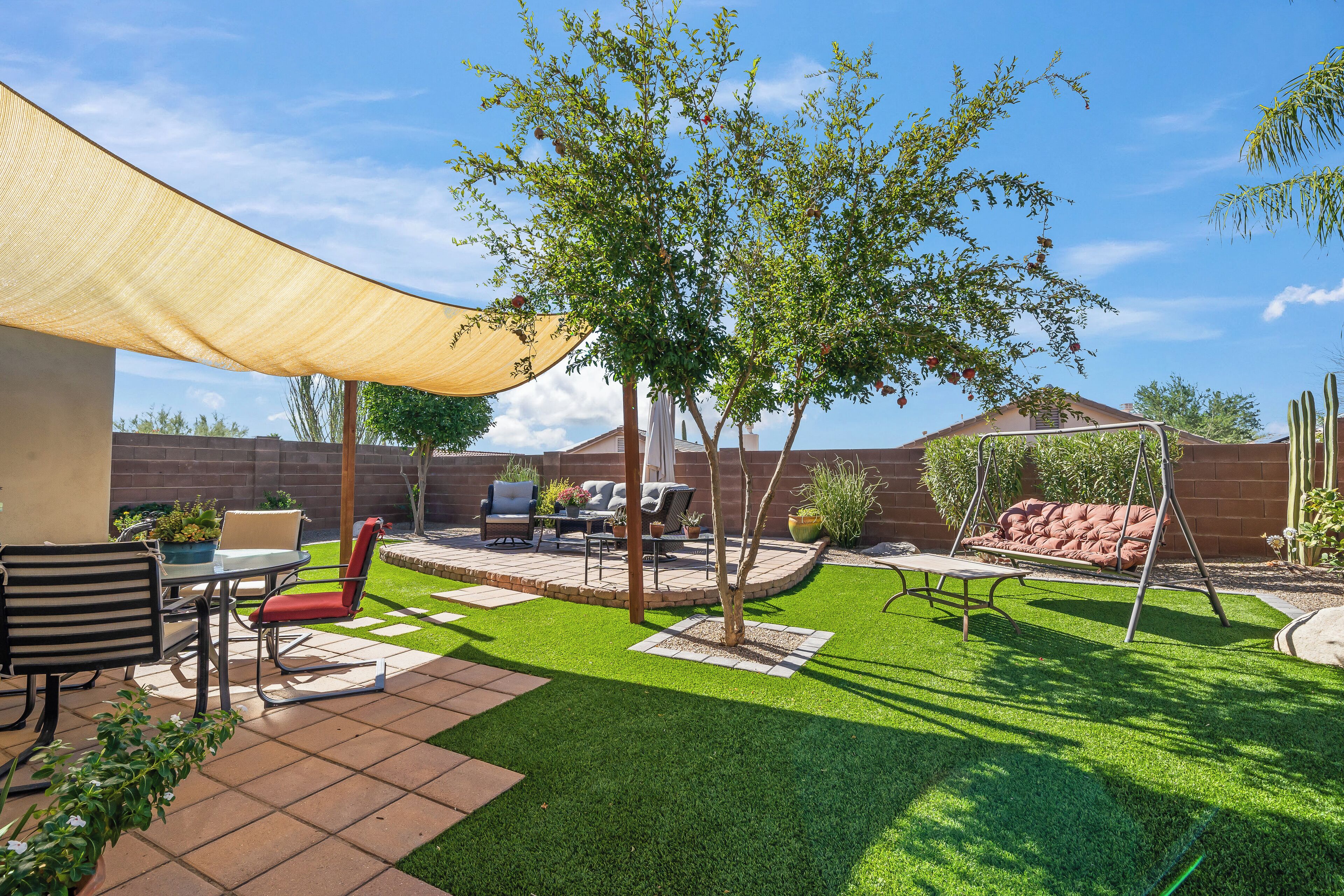 A backyard with a patio, outdoor furniture, a swing set, and a tree.