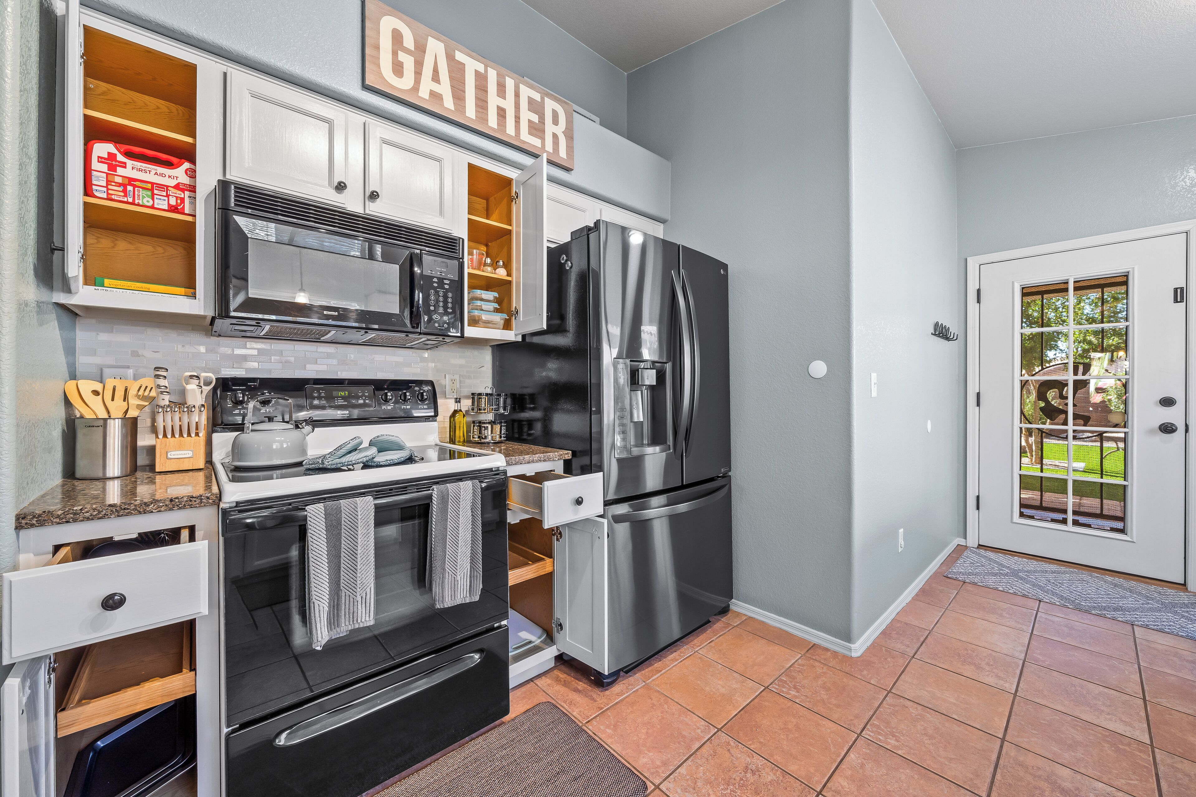 A modern kitchen with stainless steel appliances, wooden cabinets, and a 'GATHER' sign above the counter.