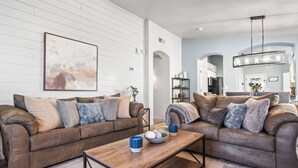A modern living room with two brown leather sofas, a wooden coffee table, and a large abstract painting on the wall. - Serene Vacation Home - Trails, Golf & Dining! (Marana)