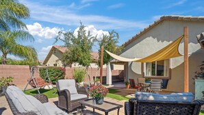 A patio area with wicker furniture, a table with a flower vase, and a swing set. - Serene Vacation Home - Trails, Golf & Dining! (Marana)