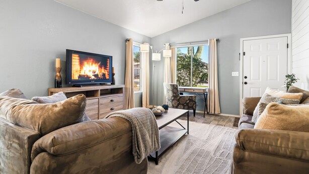 A living room with a television displaying a fire, a ceiling fan, and a view of the outdoors through a window. - Serene Vacation Home - Trails, Golf & Dining! (Marana)
