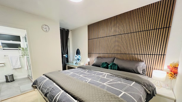 Un dormitorio moderno con cama, mesita de noche, espejo y una pared con listones de madera verticales.