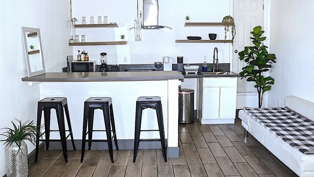 A compact kitchen with a central island, three stools, a sink, and a stove.