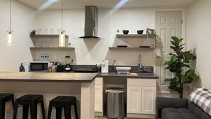 A modern kitchen with a central island, black stools, a stainless steel range hood, and a potted plant.