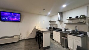 A modern kitchen with a flat-screen TV mounted on the wall, a central island with bar stools, and a stainless steel sink.