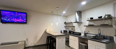 A modern kitchen with a flat-screen TV mounted on the wall, a central island with bar stools, and a stainless steel sink.