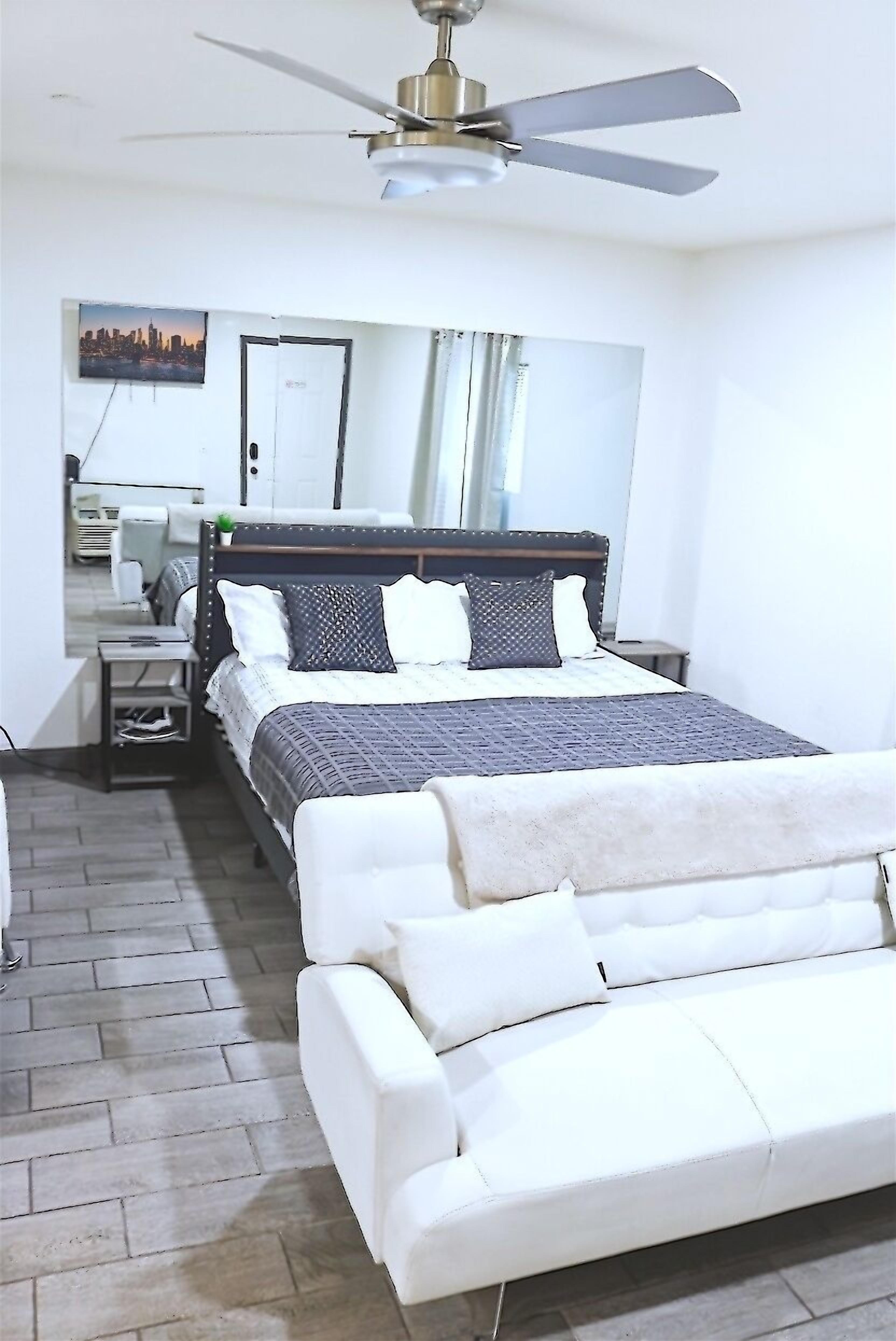 Une chambre à coucher avec un lit, un canapé blanc, un ventilateur de plafond et un tableau représentant un paysage urbain accroché au mur.