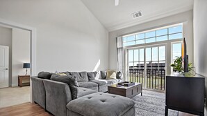 Ein geräumiges Wohnzimmer mit einem grauen Ecksofa, einem Couchtisch und einem Fernseher auf einem Standfuß.