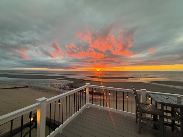 A deck with a railing overlooking a beach at sunset.