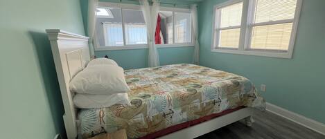 A bedroom with a bed, a bedside table, a ceiling fan, and two windows with curtains.