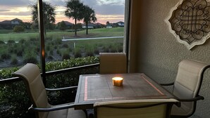 Een kamer met een groot raam met uitzicht op een golfbaan, een tafel met een kaars en een decoratief wandkunstwerk.