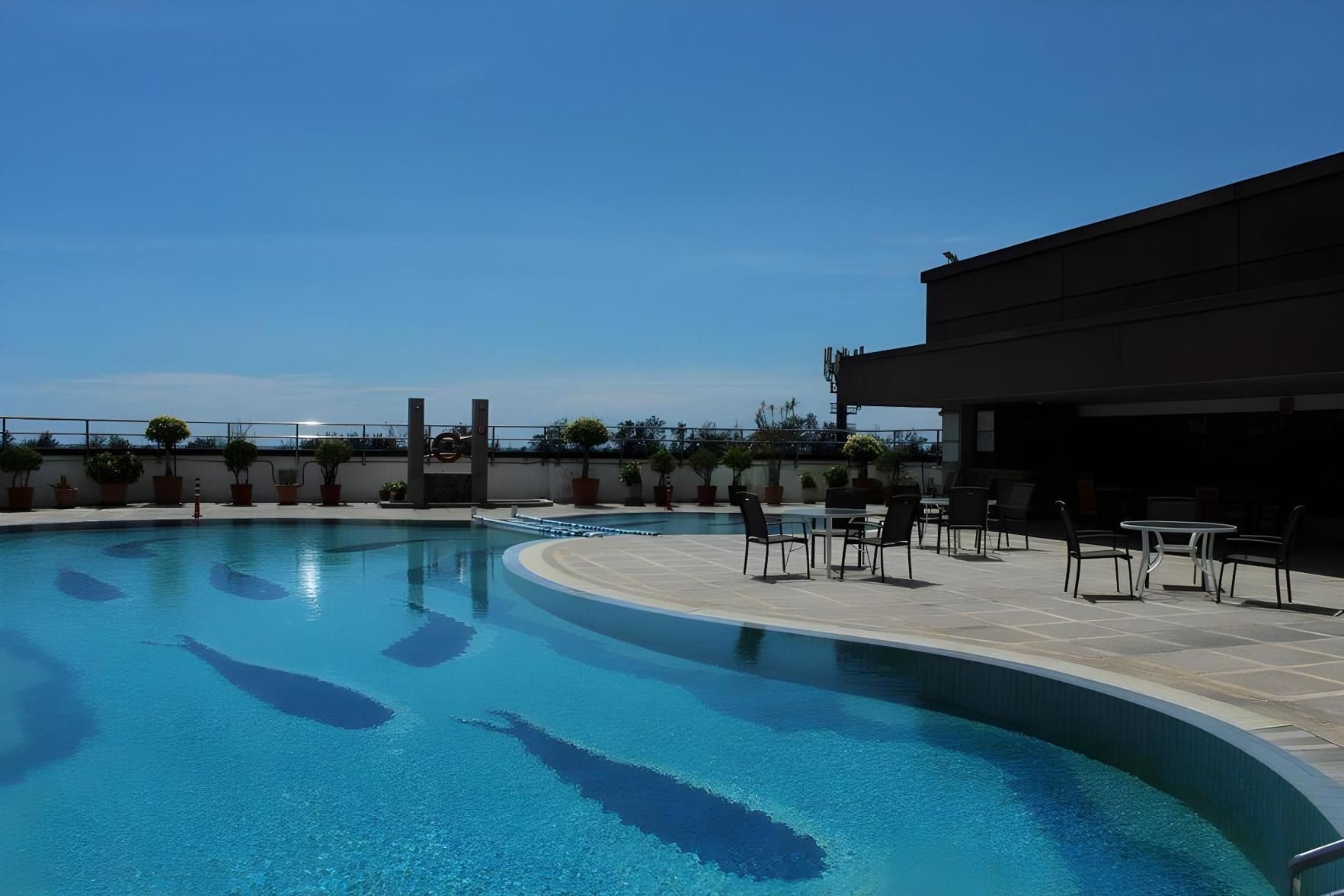 A swimming pool with a curved edge, surrounded by potted plants and outdoor seating.