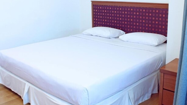 A single bed with white bedding, a wooden headboard with a patterned design, and a wooden nightstand to the right. - Imperial Hotel Miri (Miri)