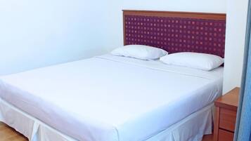 Una cama individual con ropa de cama blanca, cabecera de madera con diseño estampado y una mesita de noche a la derecha.