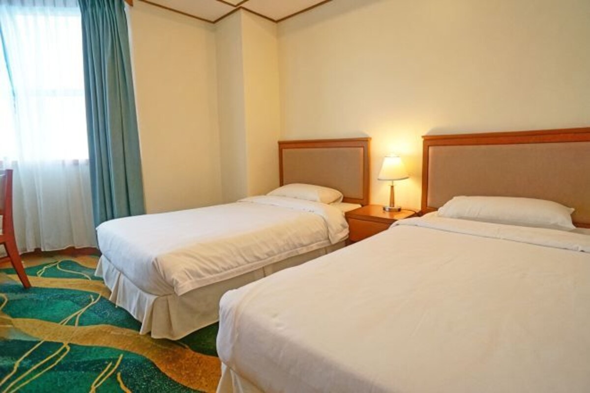 A hotel room with two beds, a nightstand with a lamp, a chair, and a window with curtains.