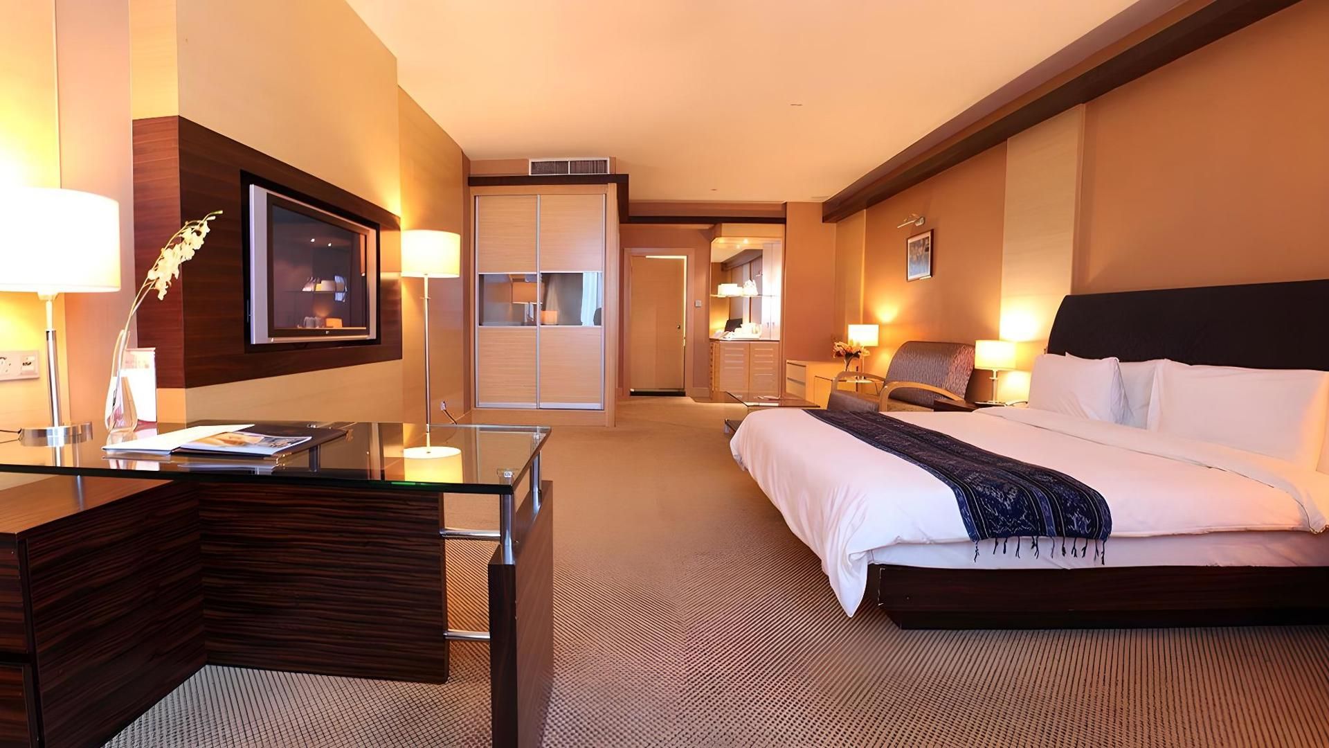 A hotel room with a bed, bedside table, lamp, and a desk with a chair.