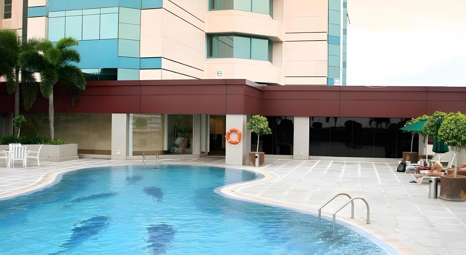 A swimming pool with a lifebuoy, surrounded by a building with large windows and a red awning.