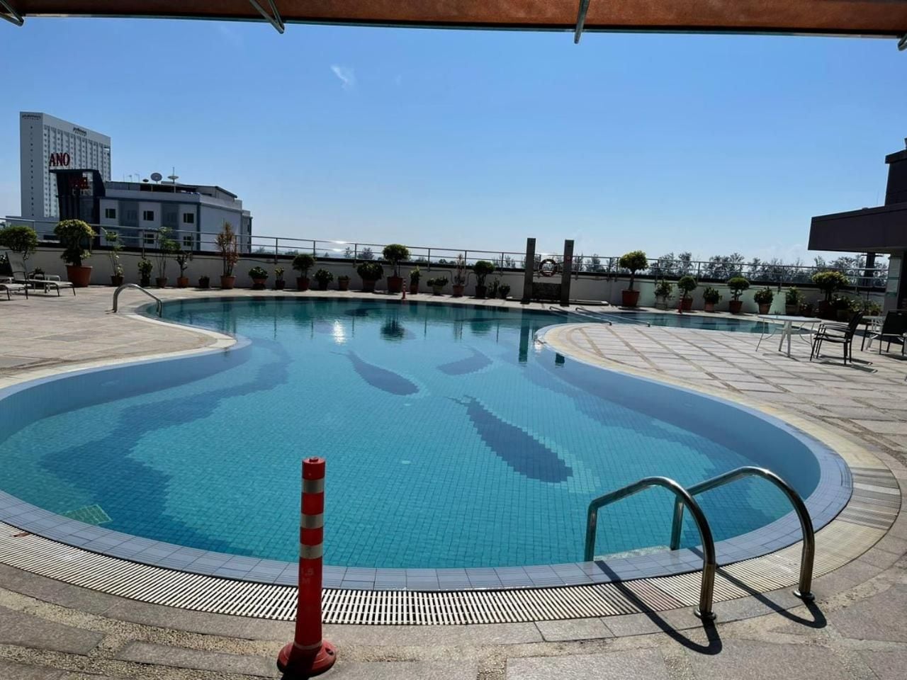 A swimming pool with a tiled deck, a safety cone, and a metal handrail.