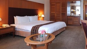 Una habitación de hotel con una cama grande, mesitas de noche, una mesa redonda de vidrio y un armario.