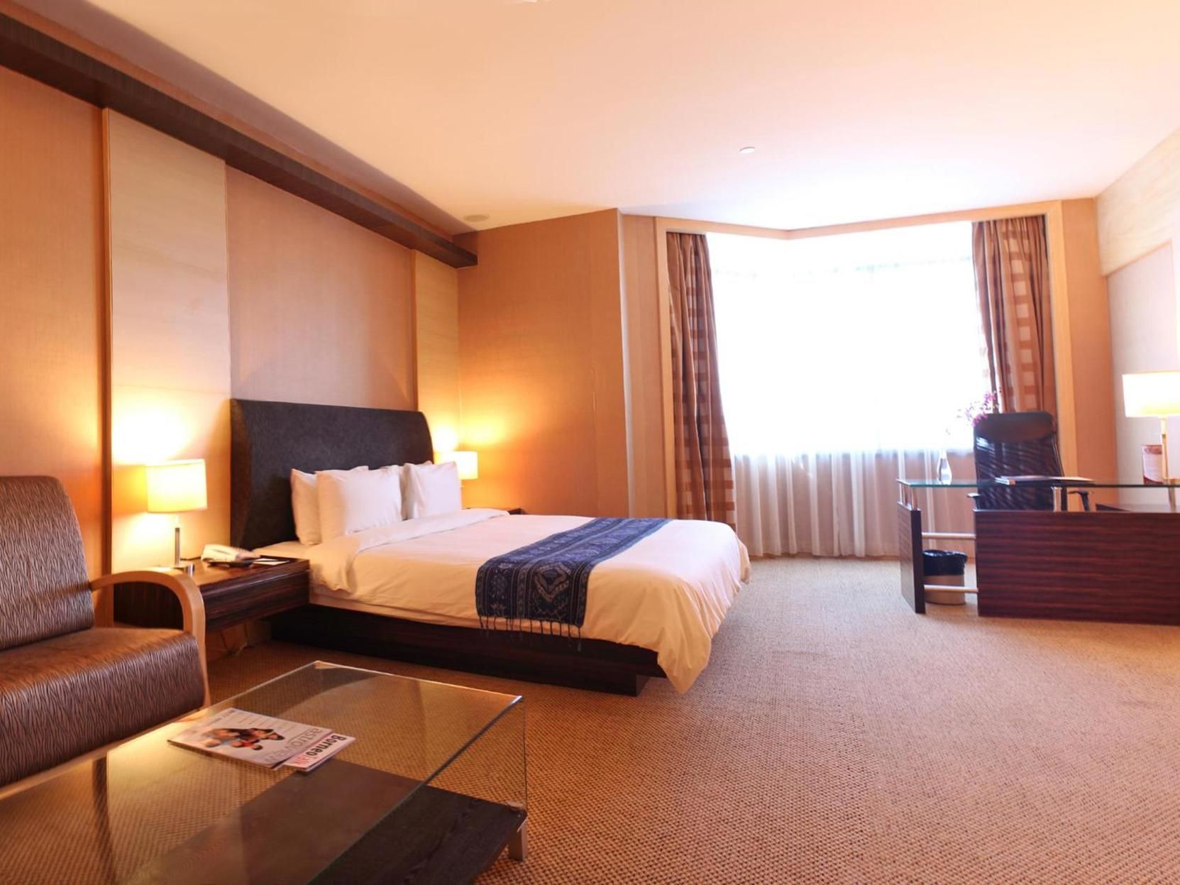 Une chambre d’hôtel avec un lit, un bureau, une chaise, une table basse et une fenêtre avec des rideaux.