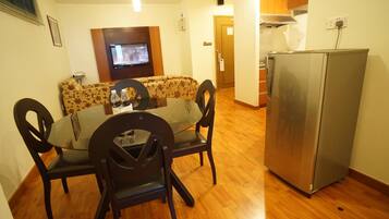 A dining area with a round table, four chairs, a sofa, a television, and a refrigerator.