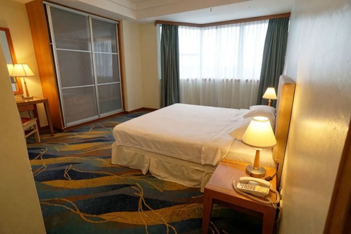 A hotel room with a bed, a desk with a lamp, a telephone, and a sliding door.