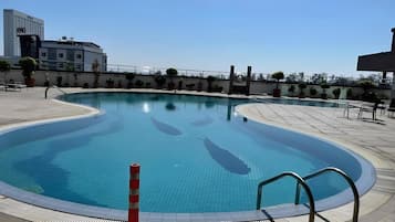 A swimming pool with a tiled deck, a safety barrier, and potted plants around the perimeter.